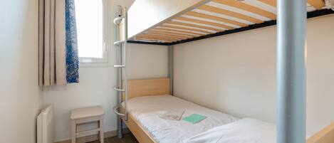 A bunk bed room with a window, a radiator, a small stool, and a ladder.