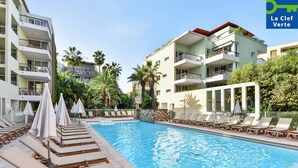 A swimming pool with lounge chairs and umbrellas, surrounded by multi-story buildings with balconies and palm trees. - Résidence Pierre & Vacances Premium Port-Prestige (Antibes)