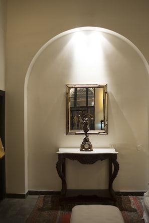 Un pasillo con pared blanca, un arco de entrada, un espejo, una mesita con un reloj y una alfombra estampada.