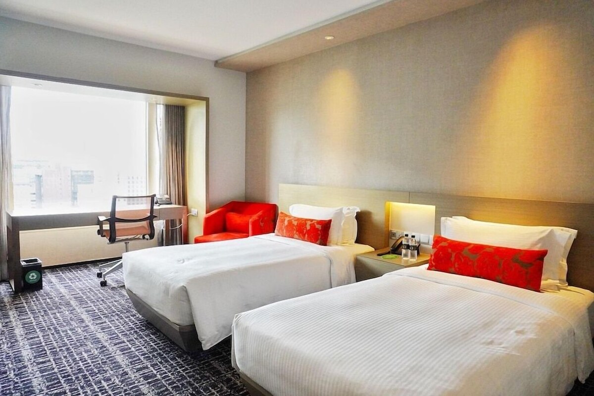 Une chambre d’hôtel avec deux lits, un bureau, une chaise et une fenêtre donnant sur un beau paysage.
