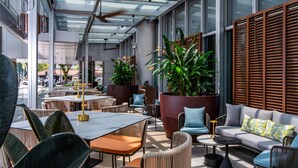 An outdoor seating area with tables, chairs, and a sofa, surrounded by large potted plants and wooden slats. - Carlton Hotel Singapore (Singapore)