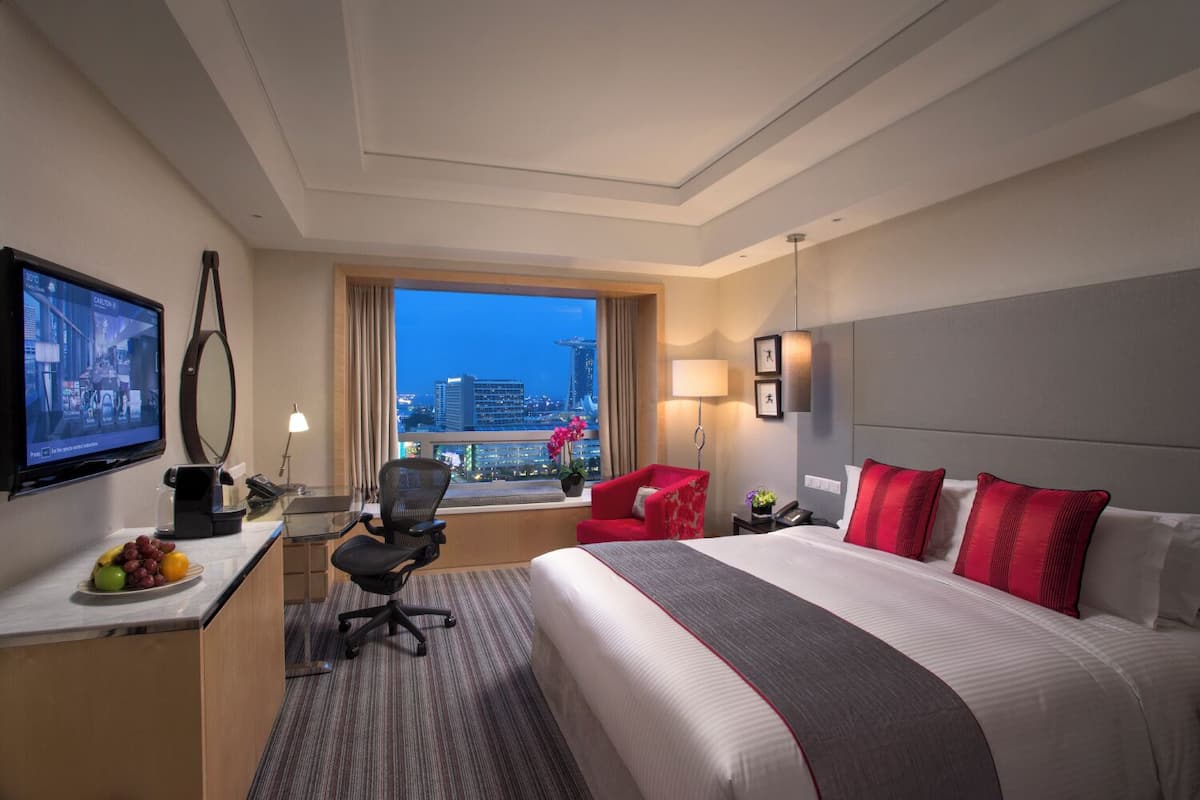 Une chambre d’hôtel équipée d’un lit, d’un bureau, d’une chaise, d’une télévision et offrant une vue sur le paysage urbain.