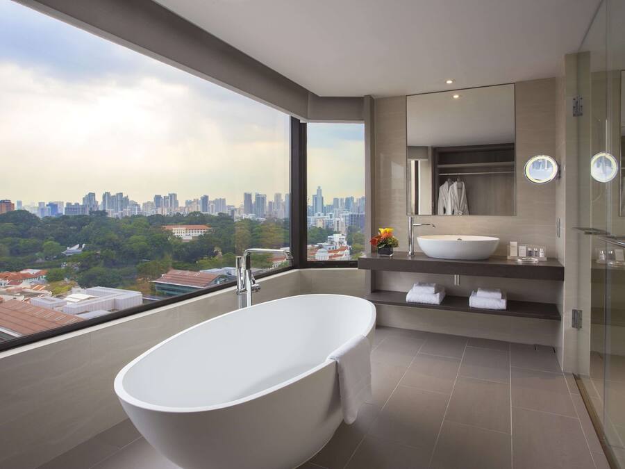 Un baño moderno con una bañera independiente, un espejo grande y vistas a un paisaje urbano.