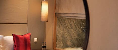 A hotel room with a bed, a nightstand, a lamp, and a mirror reflecting part of the room.