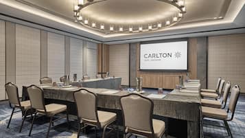 Una sala de conferencias con una mesa larga, sillas, una pantalla de proyector que muestra 'Carlton Hotel Singapore' y una lámpara de araña moderna.