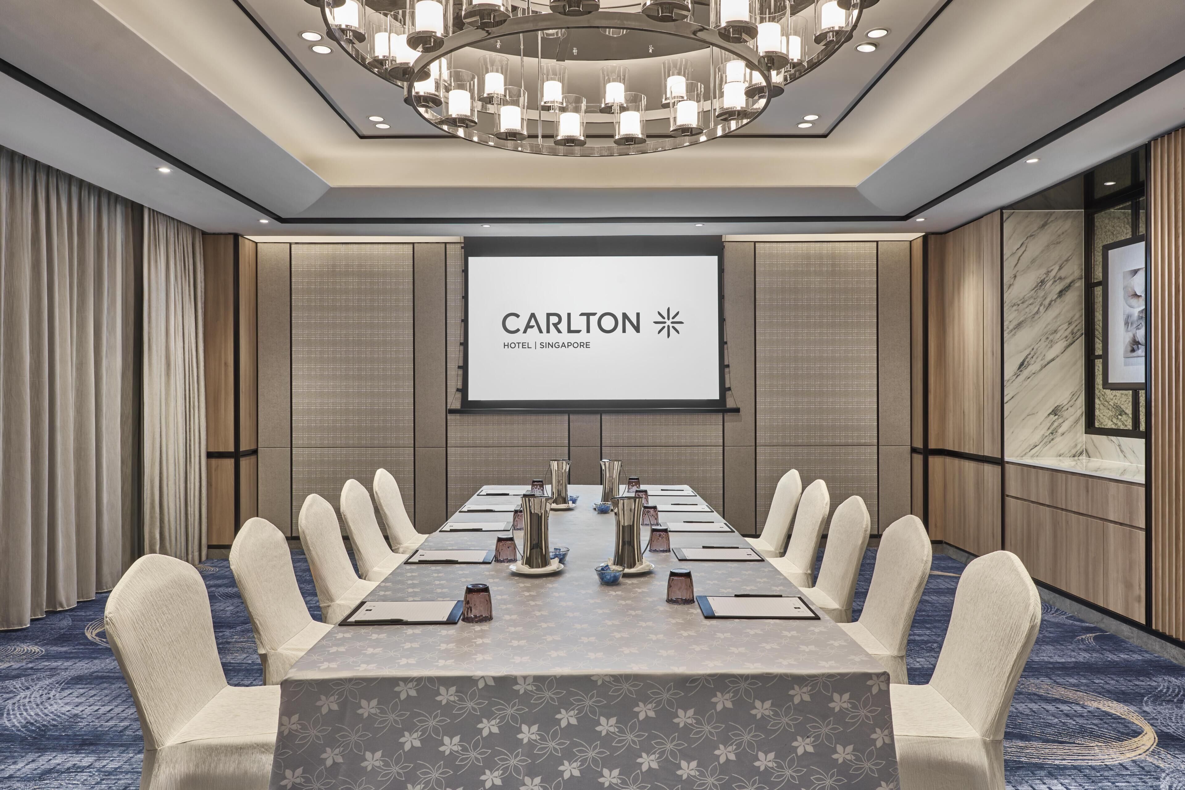 A conference room with a long table, chairs, a projector screen, and a chandelier.