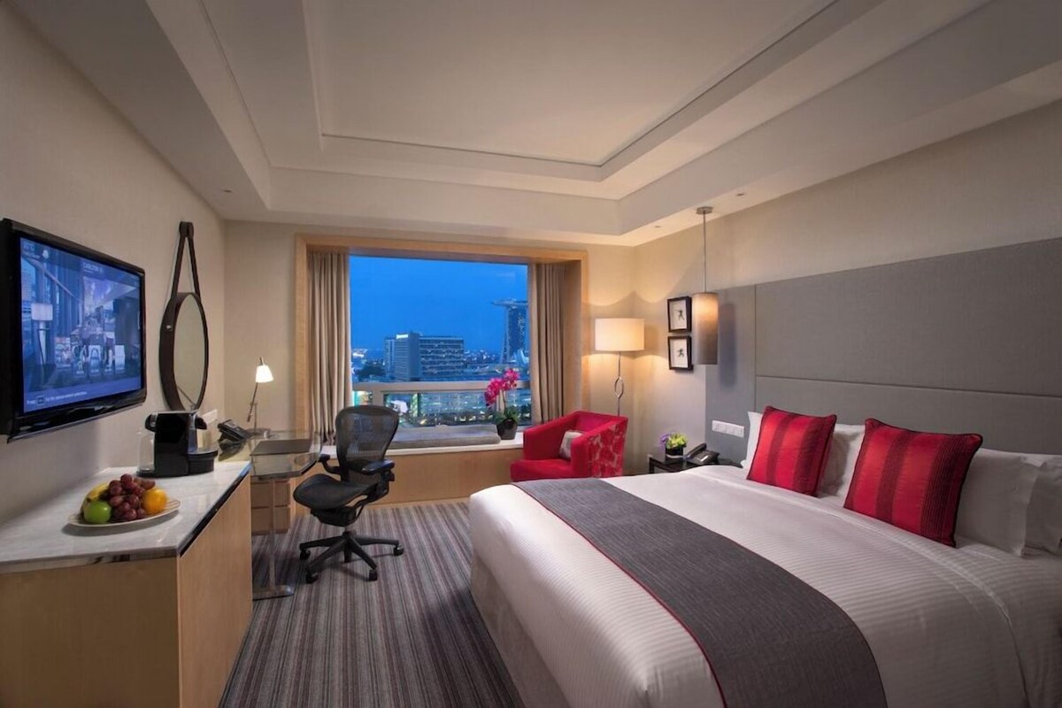 Une chambre d’hôtel avec un grand lit, un bureau avec un ordinateur, une télévision et une fenêtre donnant sur la ville.