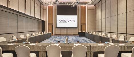 Un salón de conferencias con una larga mesa, sillas y una pantalla mostrando 'Carlton Hotel Singapore'.