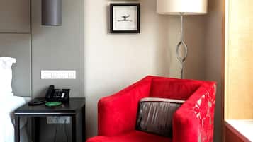 Una habitación de hotel con un sillón rojo, un escritorio con teléfono, obras de arte enmarcadas en la pared y una lámpara de pie.