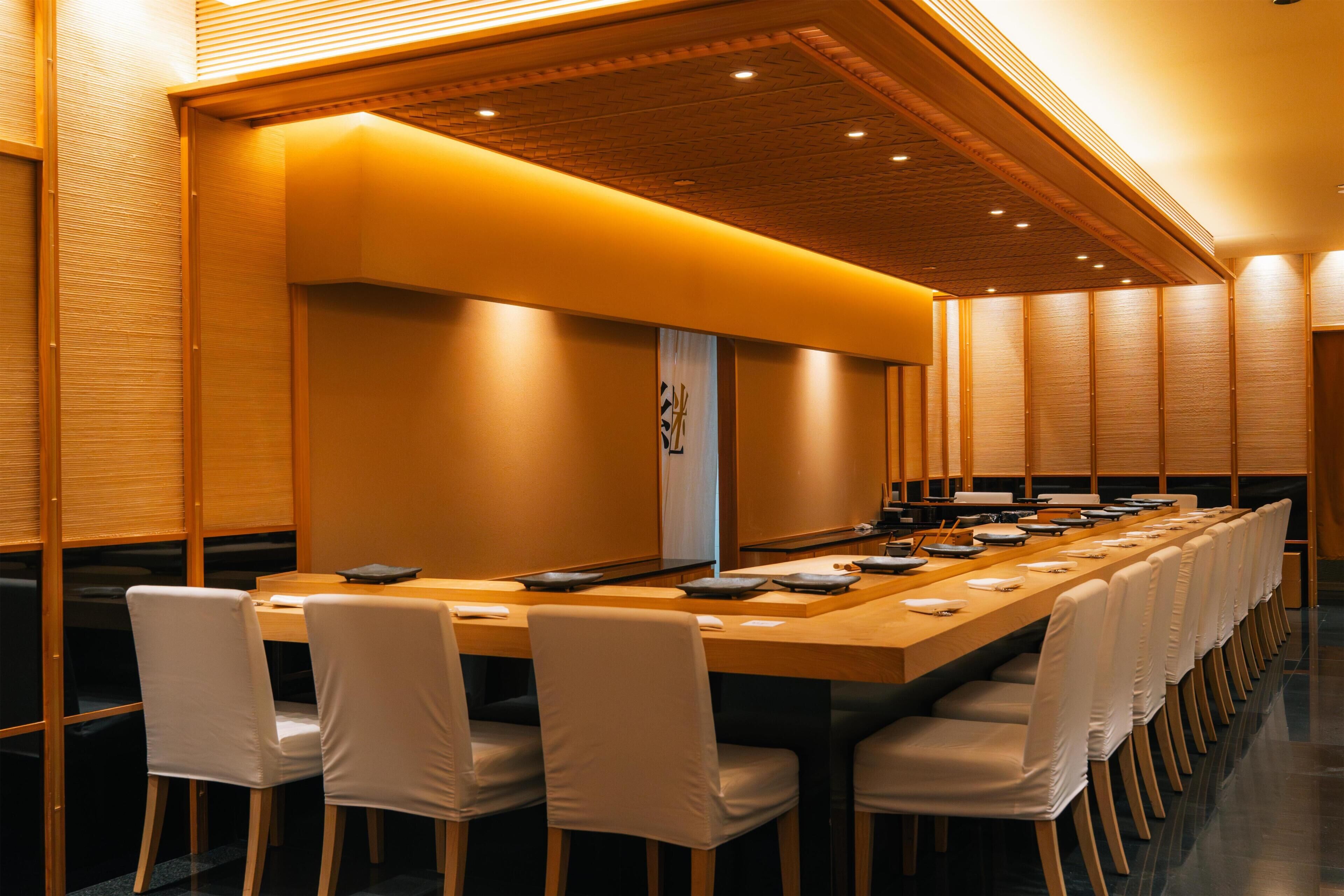 Une salle de conférence avec une longue table, des chaises blanches et un plafond en bois.