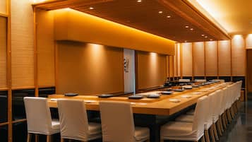 Une salle de conférence avec une longue table, des chaises blanches et un plafond en bois.