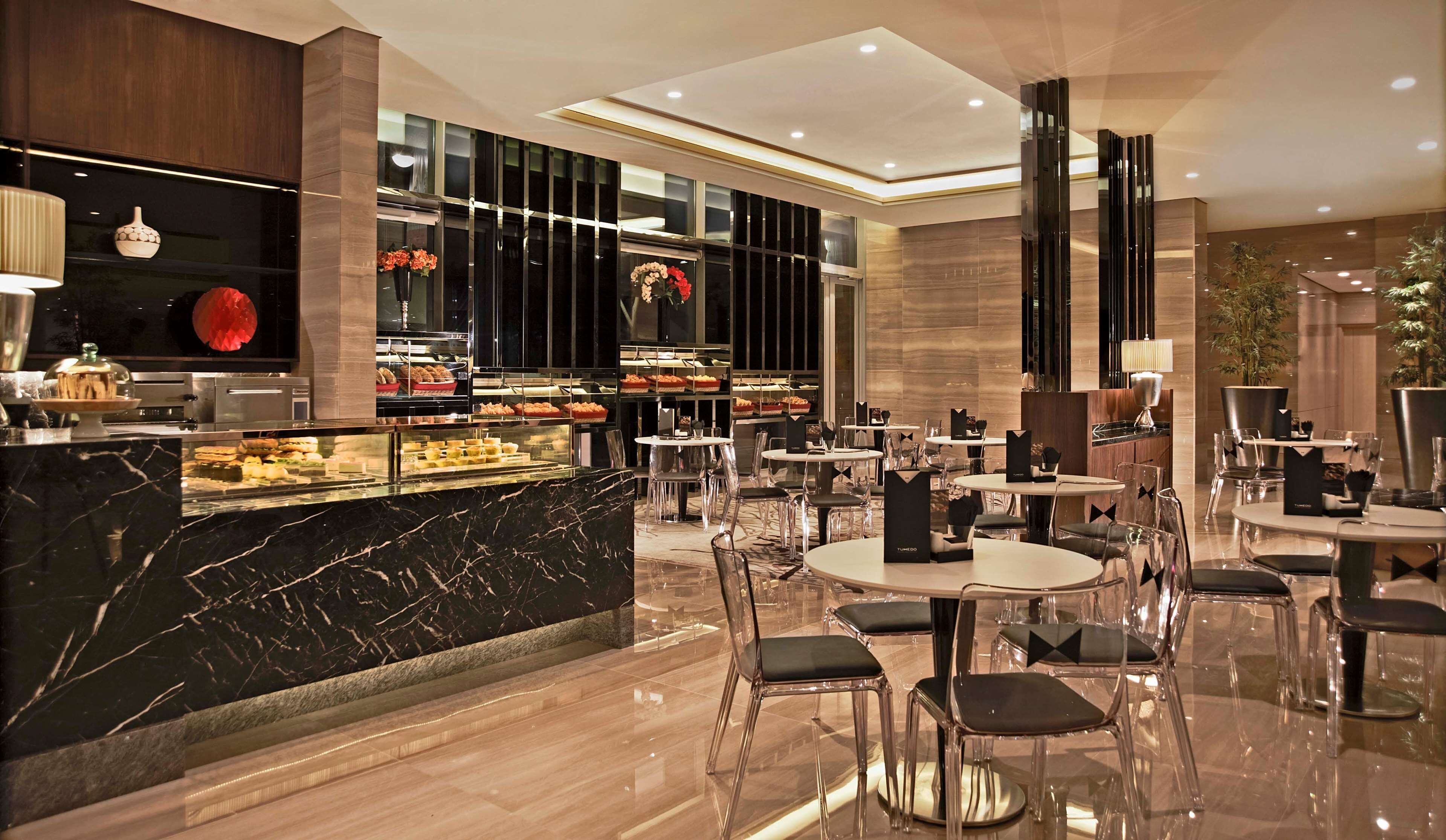 A modern hotel lobby with marble flooring, a central counter with a display case, and multiple seating areas with clear chairs.