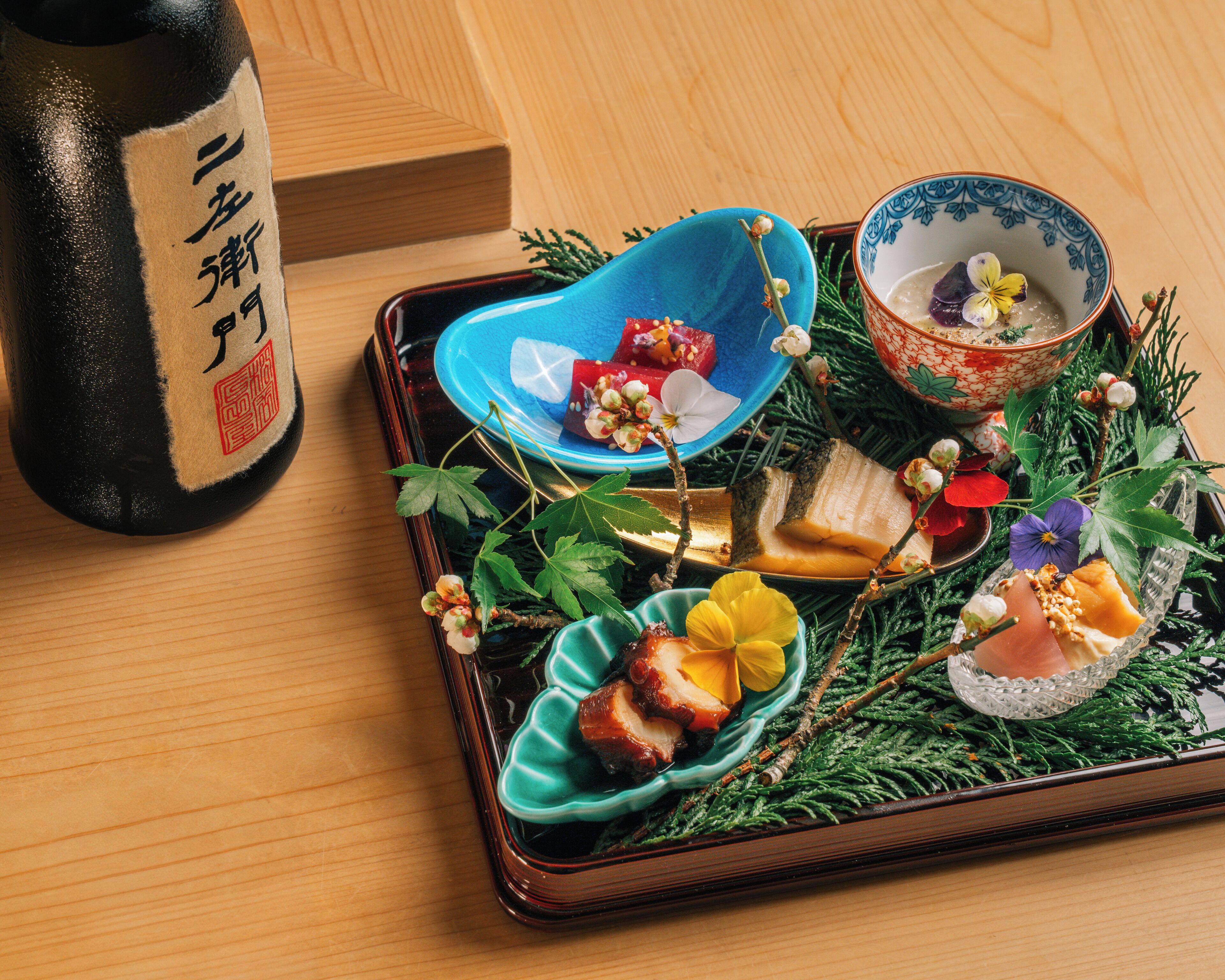 Een dienblad met eten en drinken, waaronder een fles met Japanse tekens, op een houten tafel.