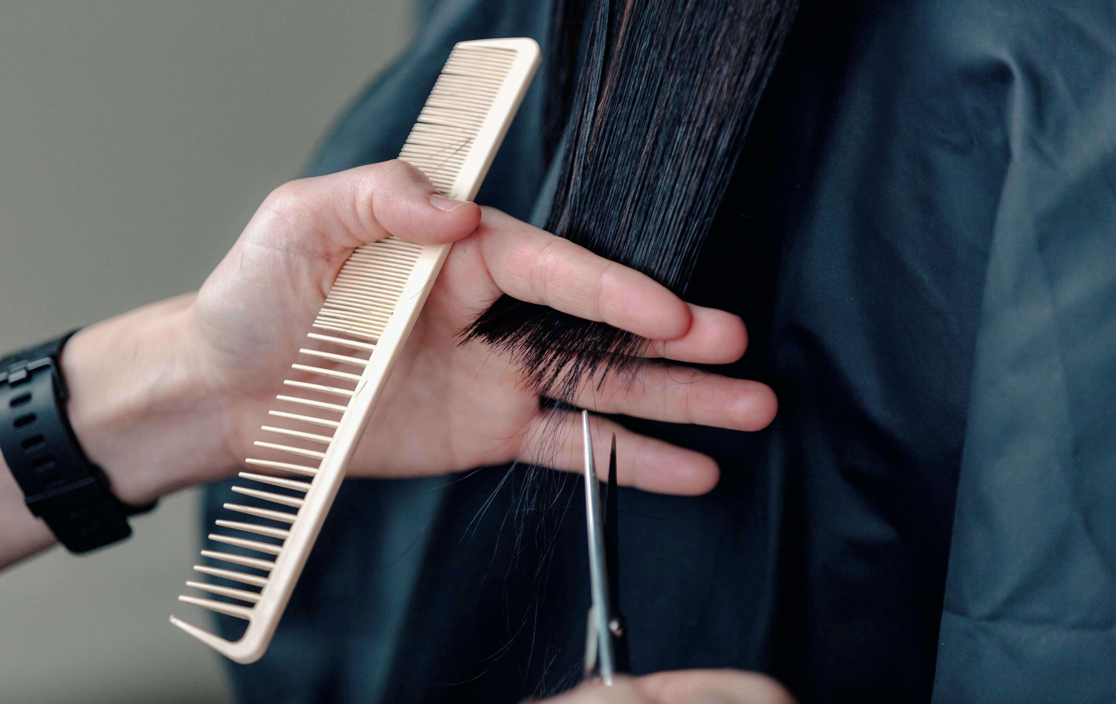 A person holding a comb and scissors, likely performing a hair styling or grooming task.