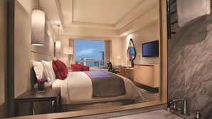 A hotel room with a large bed, a desk, a chair, a TV, a bathroom with a bathtub, and a view of the city. - Carlton Hotel Singapore (Singapore)