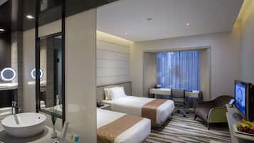 Ein Hotelzimmer mit einem großen, runden Waschbecken, zwei Betten, einem Schreibtisch mit Stuhl, einem Fernseher und einem Fenster mit Vorhängen.