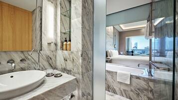 A modern bathroom with a marble sink, a glass shower enclosure, and a view of a cityscape through a large window.
