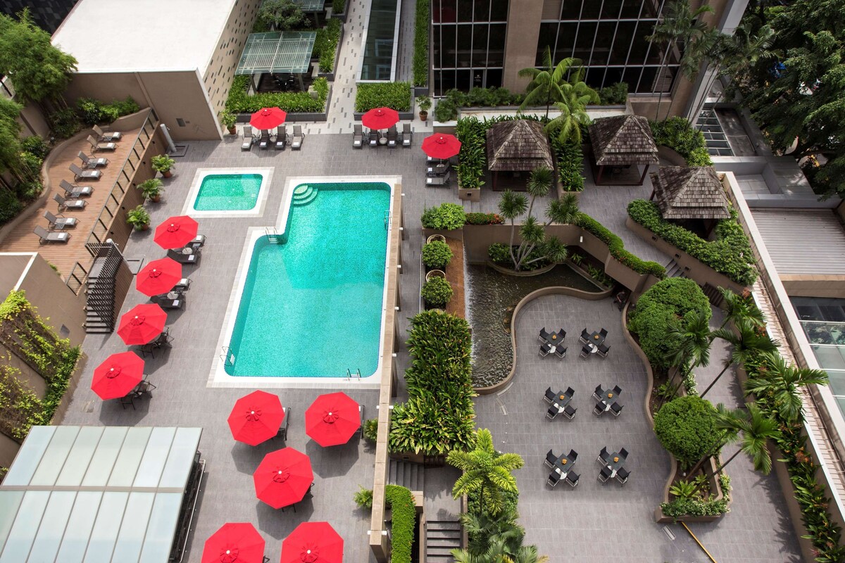 Vue aérienne d’un hôtel doté de deux piscines, de chaises longues et de parasols rouges.