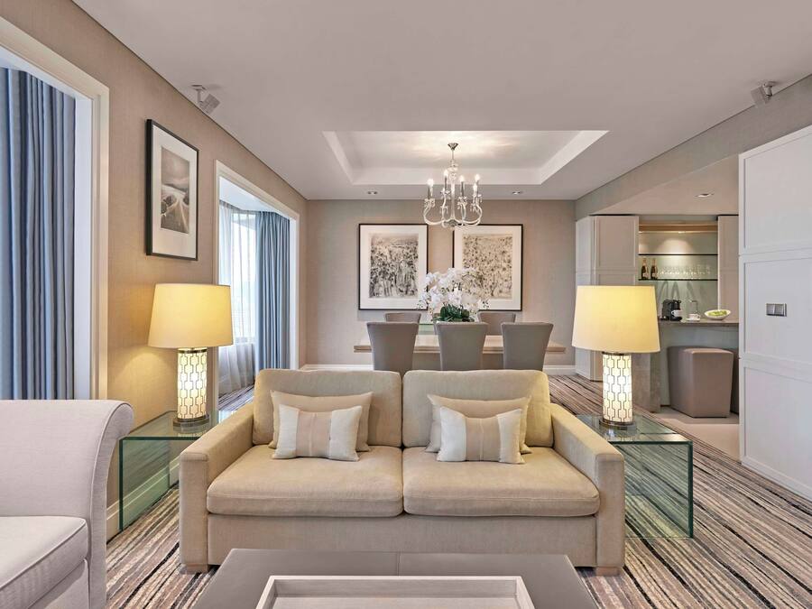 A modern hotel room with a sofa, two lamps, a dining table, and artwork on the walls.