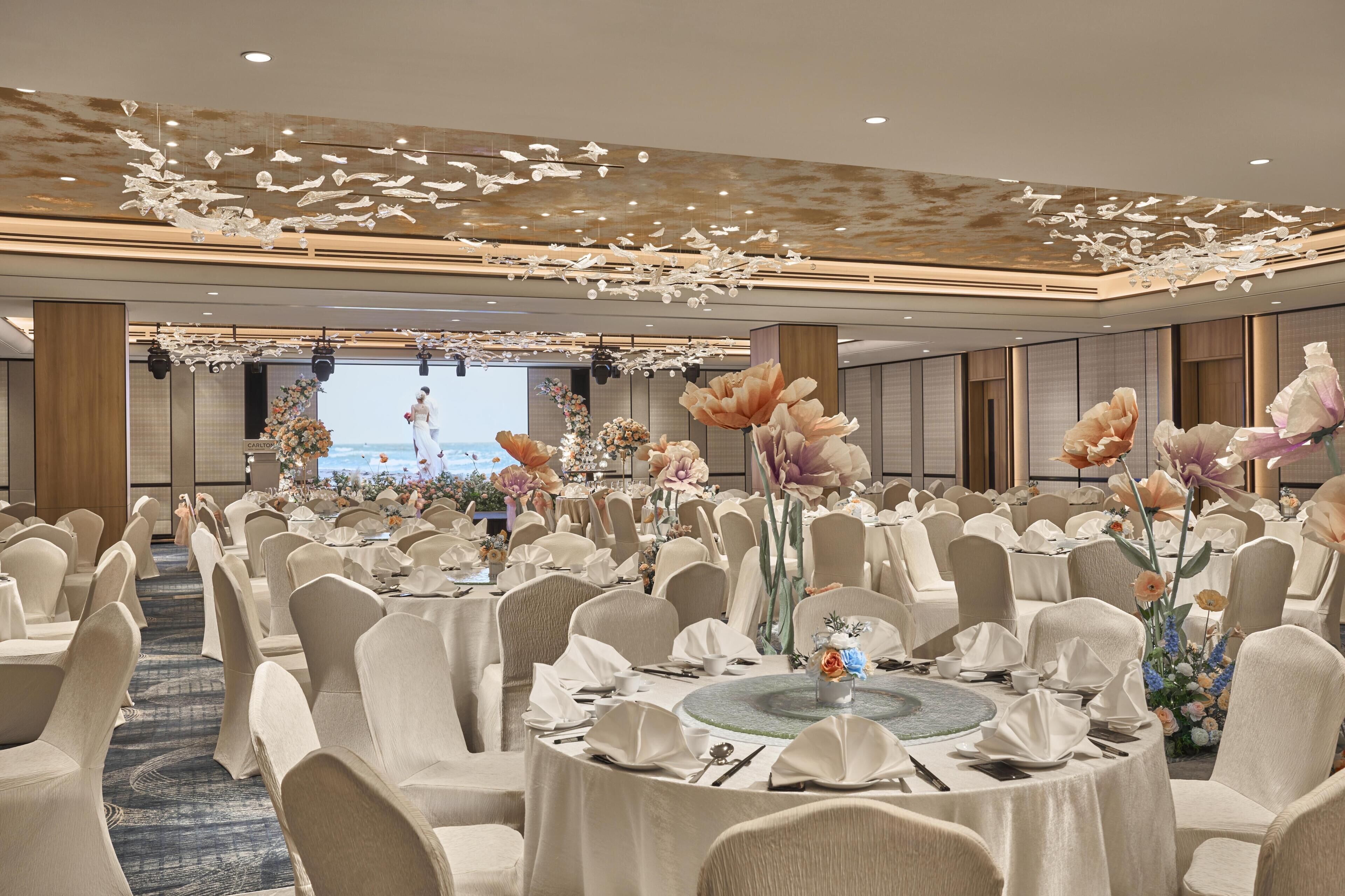 A banquet hall with round tables, white chairs, and floral centerpieces.