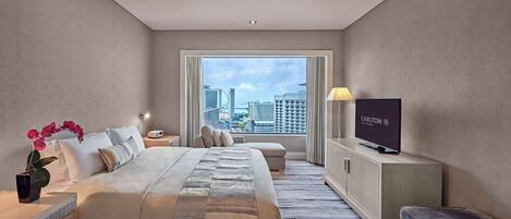 A hotel room with a bed, a TV, a desk, and a view of the city.