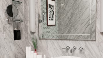 A modern bathroom with a marble vanity, a large mirror, a framed artwork, and a glass shower enclosure.