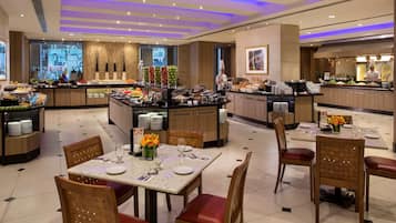 A hotel dining area with a buffet, multiple dining tables, and chairs.