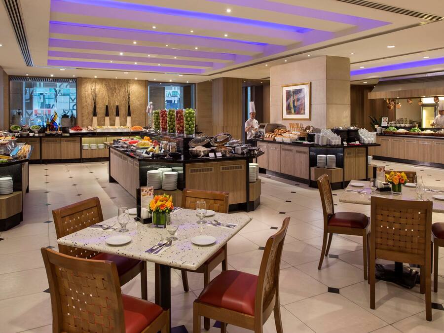 A hotel dining area with a buffet, multiple dining tables, and chairs.