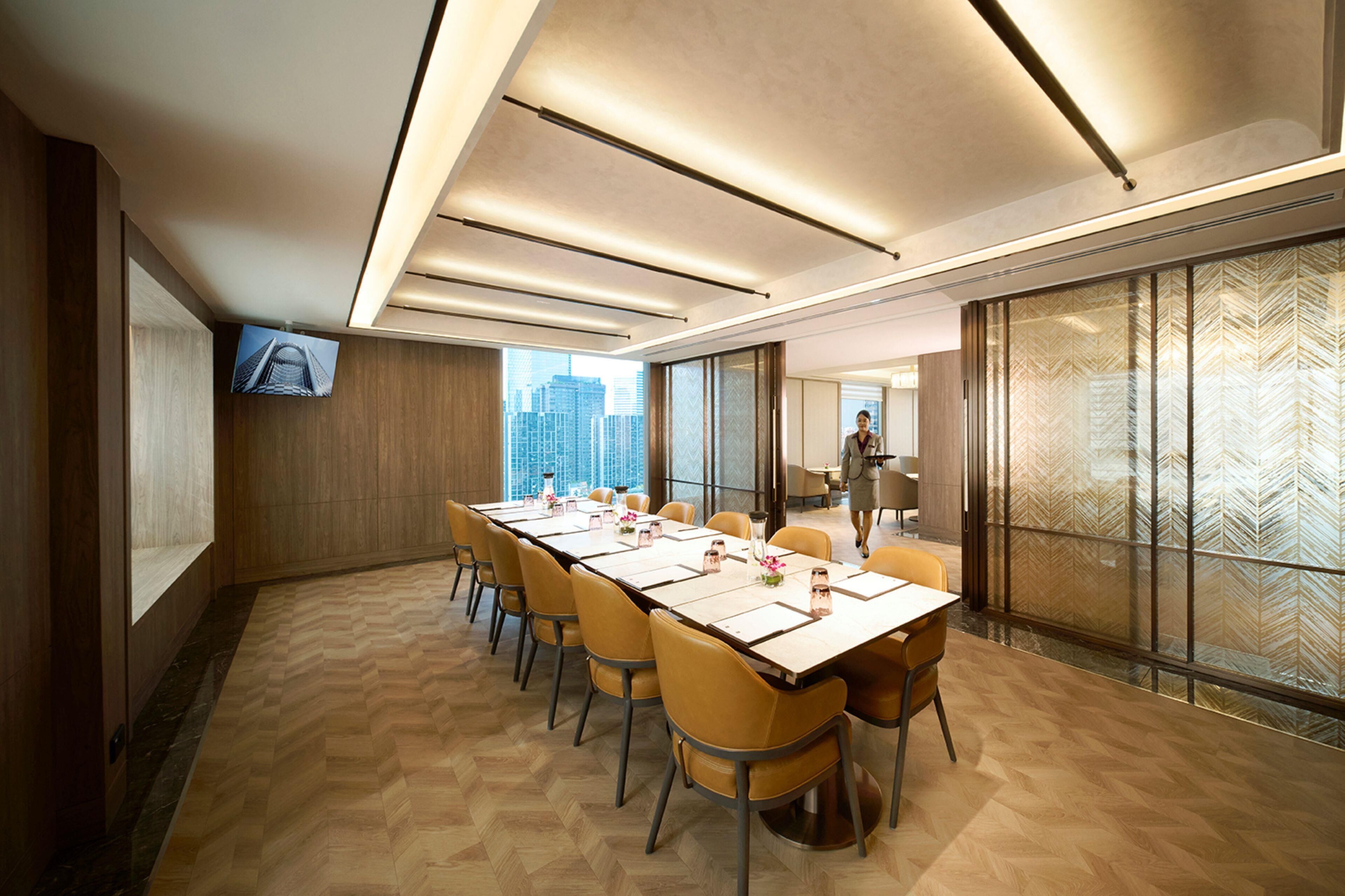 Un salón de conferencias con una mesa larga, sillas, una televisión y vistas a la ciudad a través de amplias ventanas.