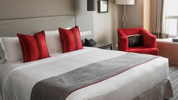 A hotel room with a large bed, a red chair, a desk with a phone, and a lamp.