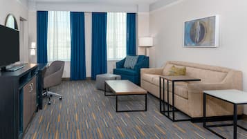 Une chambre d’hôtel équipée d’un téléviseur à écran plat, d’un bureau, d’un canapé, d’une table basse et d’une grande fenêtre avec des rideaux bleus.