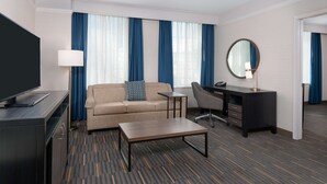 A hotel room with a sofa, a desk, a chair, a television, and a large mirror. - Hampton Inn & Suites Buffalo Downtown (Buffalo)