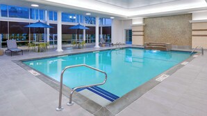 An indoor swimming pool with clear blue water, a metal pool ladder, and a seating area with tables and chairs. - Hampton Inn & Suites Buffalo Downtown (Buffalo)
