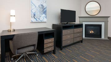 A hotel room with a desk, chair, television, fireplace, and artwork on the wall.