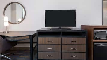Ein Hotelzimmer mit Schreibtisch, Flachbildfernseher, Holzkommode, Lampe, Mikrowelle und einem kleinen Kühlschrank.