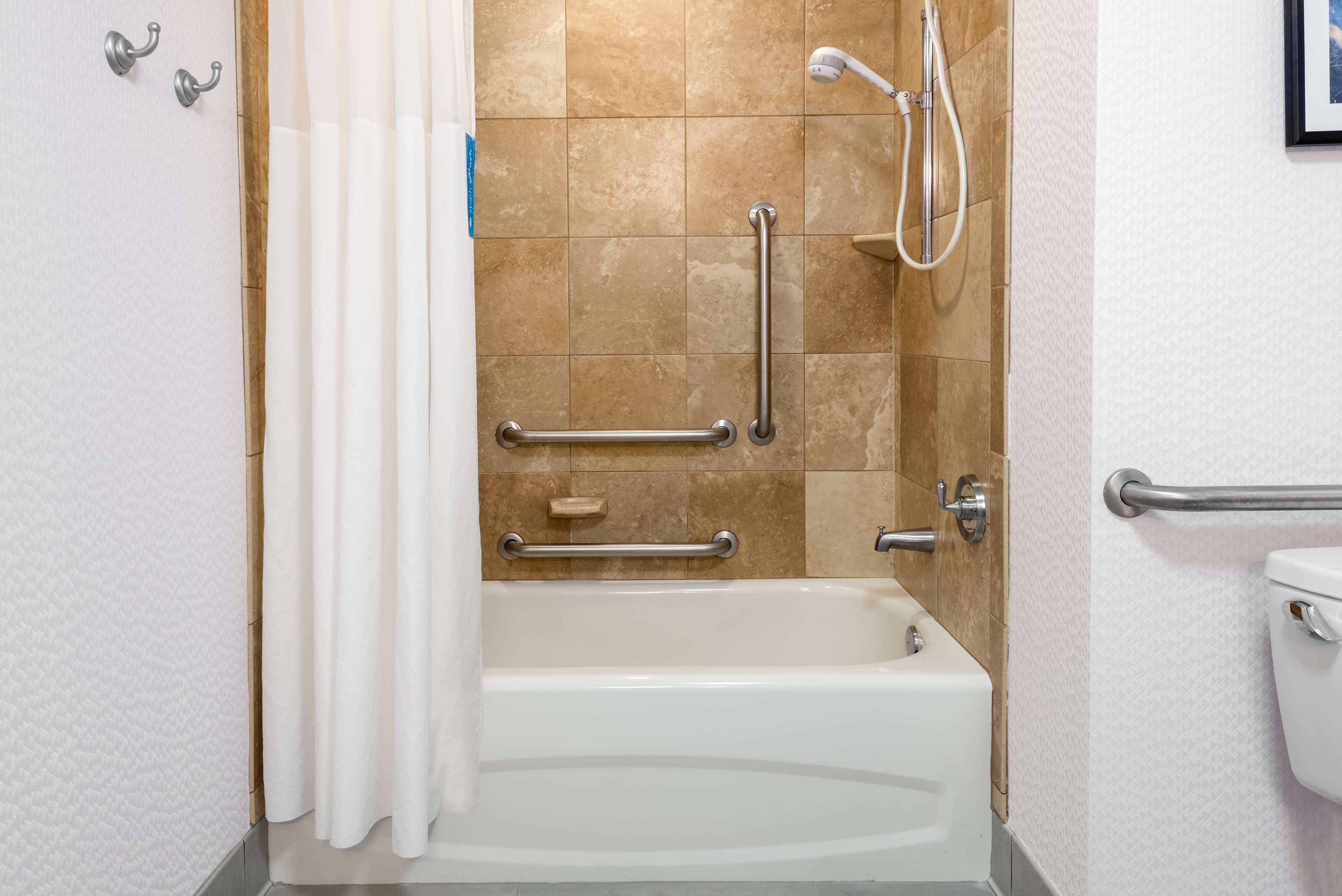 A bathroom with a bathtub, grab bars, and a shower head.