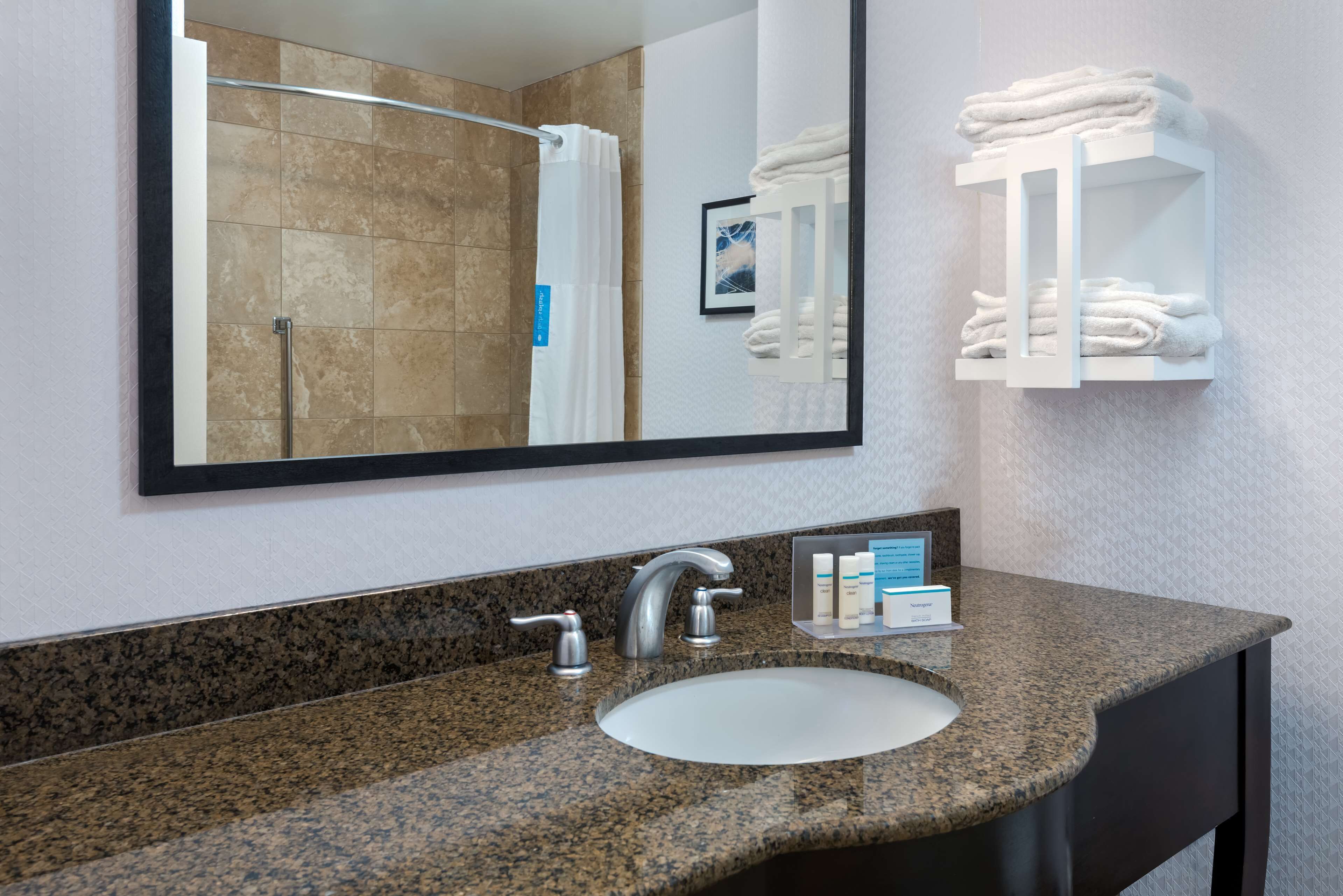 A bathroom with a granite countertop, a white sink, a large mirror, and a towel rack with folded towels.