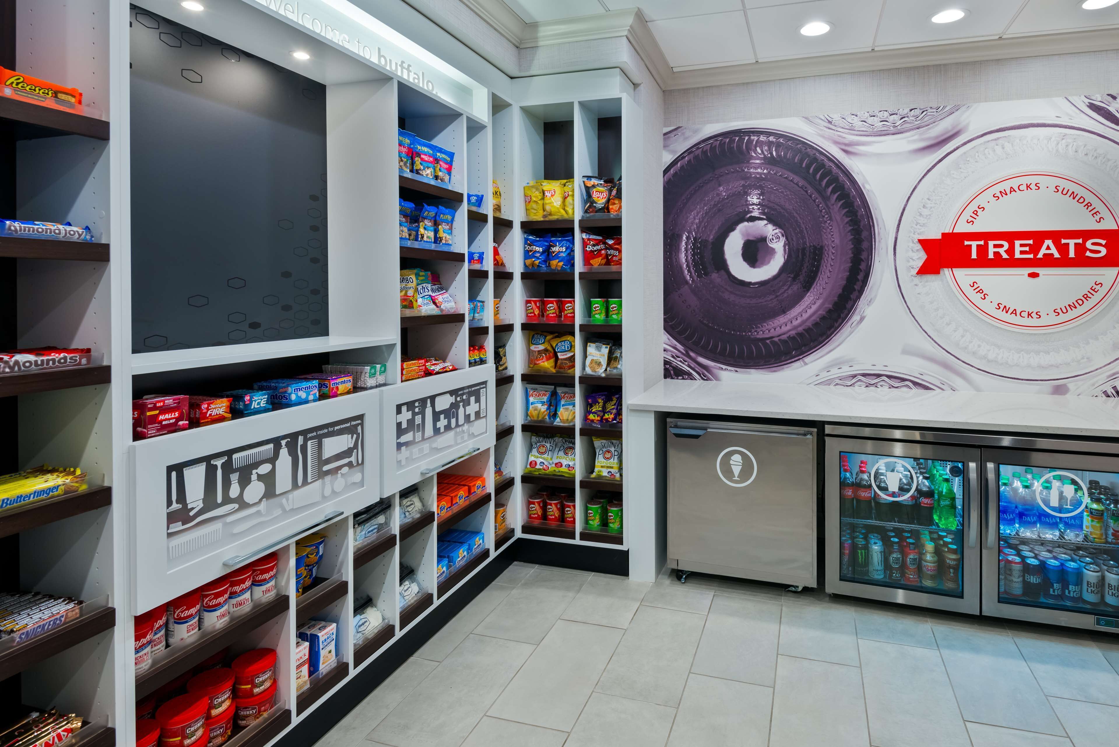 Un espace dédié aux collations et aux gourmandises, avec des étagères remplies de divers produits, un présentoir réfrigéré et une fresque murale faisant la publicité de ces gourmandises.
