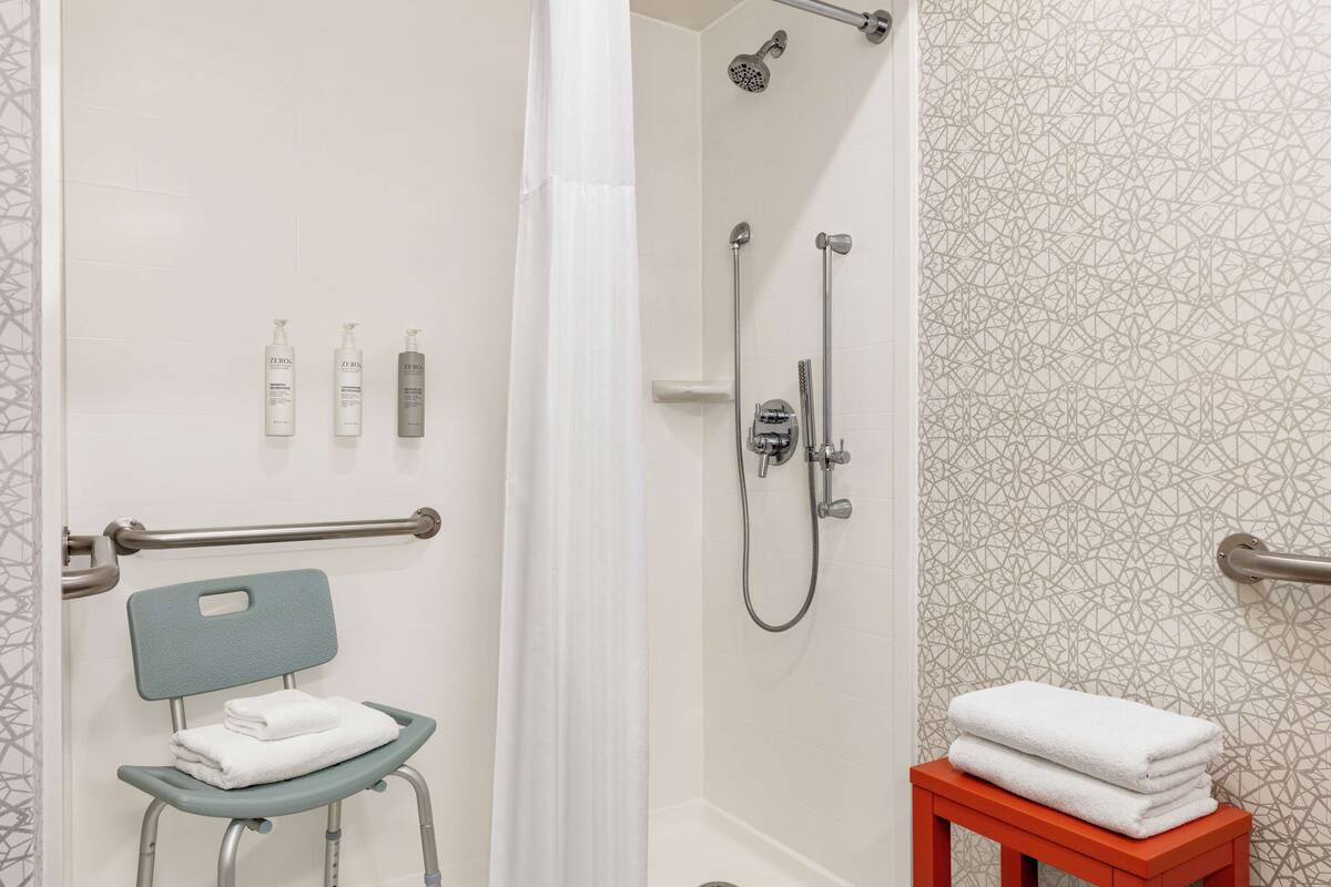 A shower area with a glass door, a handrail, a showerhead, and a towel rack.