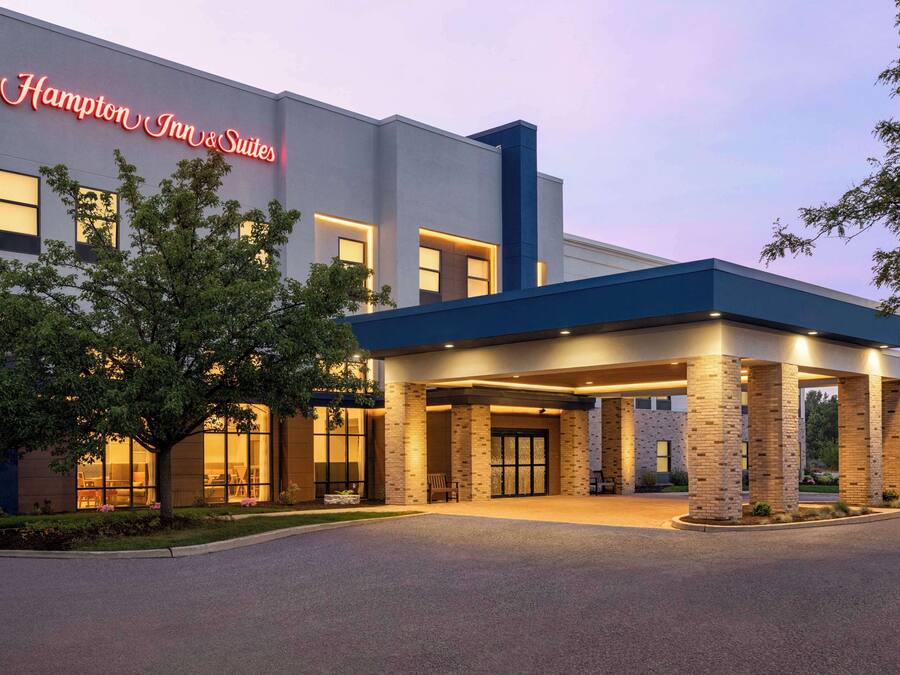 A modern Hampton Inn & Suites building with a well-lit entrance and a large tree in front.