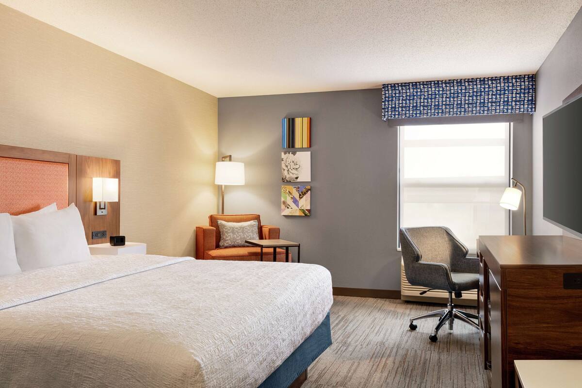 A hotel room with a large bed, a desk, a chair, and a window with a view.