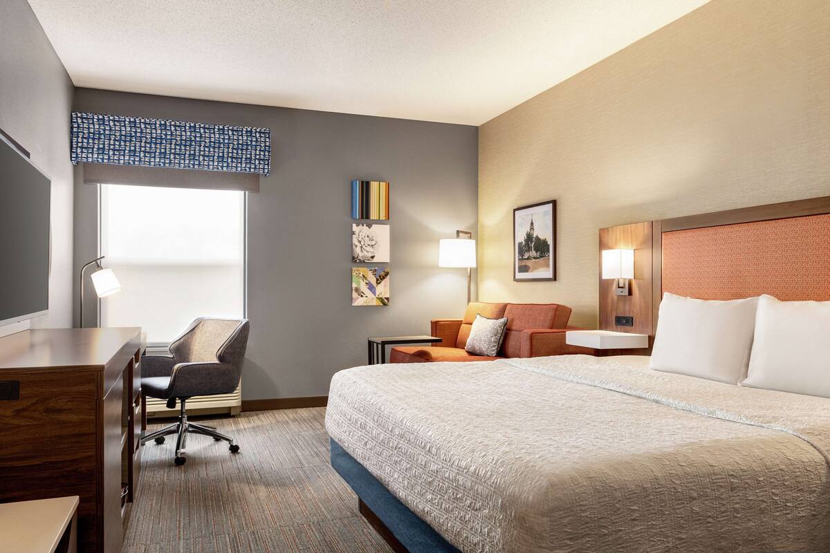 A hotel room with a large bed, a desk with a chair, a small table, and a window with a view.