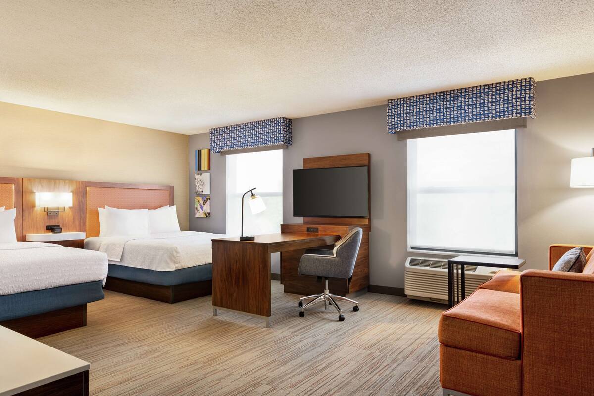 A hotel room with two beds, a desk, a chair, a TV, and a couch.