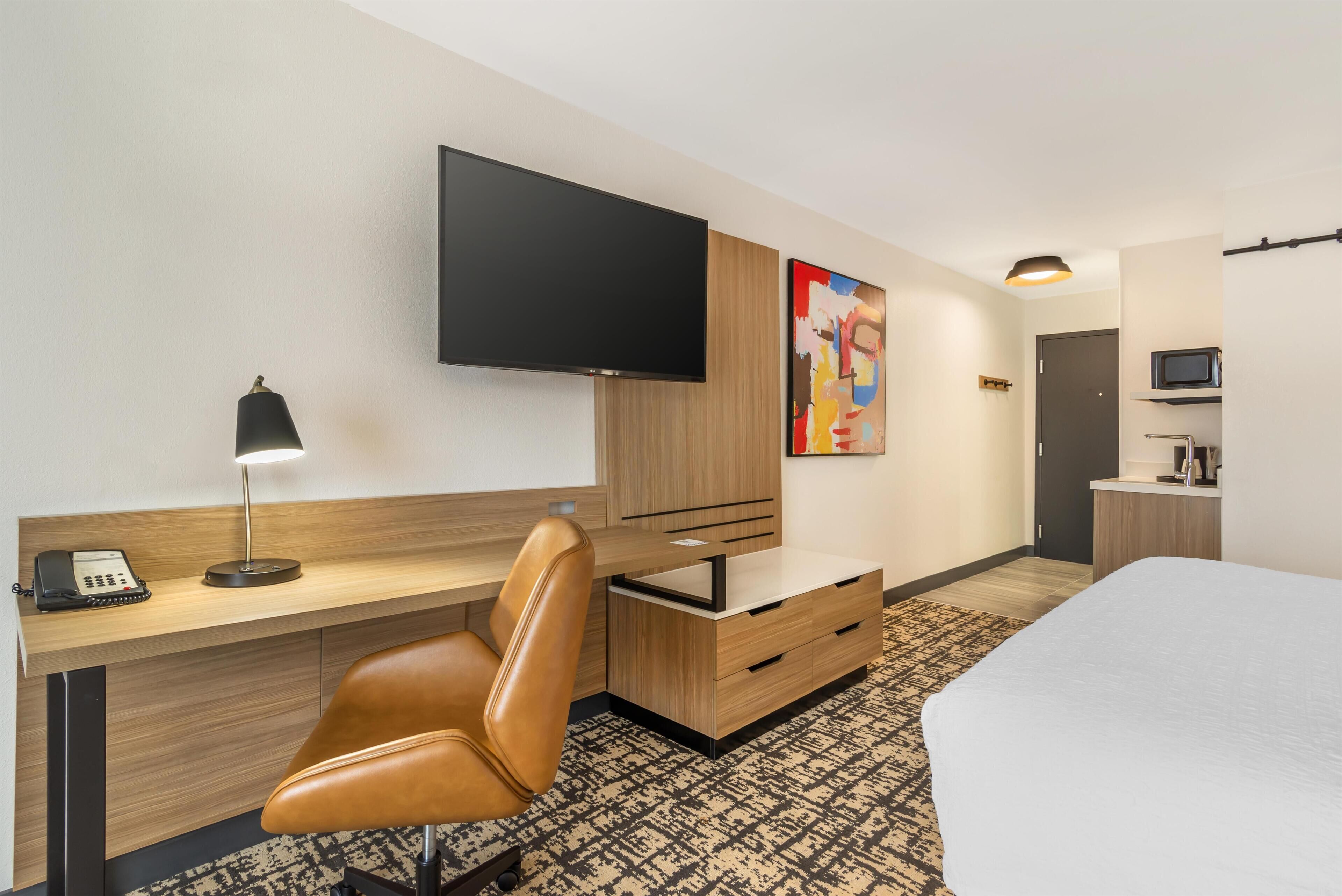 Hotellihuone, jossa on sänky, työpöytä tuolilla, televisio, puhelin, mikroaaltouuni ja taulu seinällä.