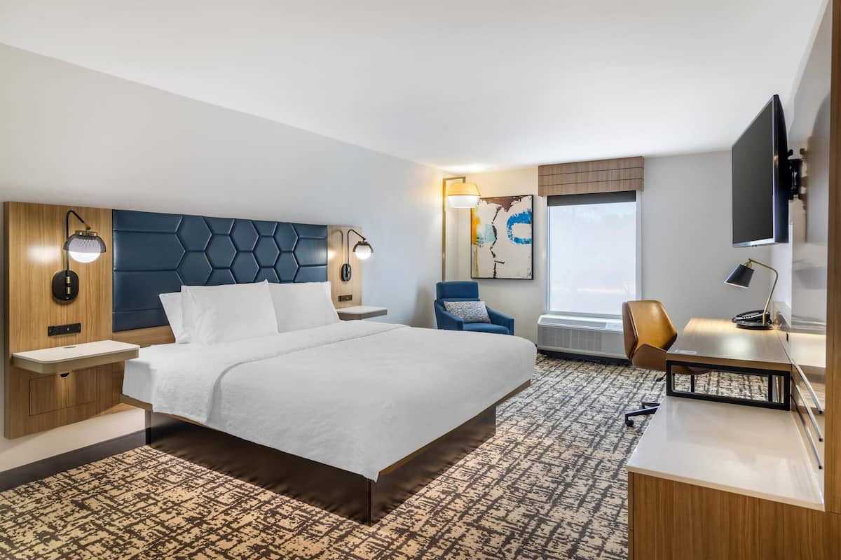 A hotel room with a large bed, a desk, a chair, a TV, and a painting on the wall.