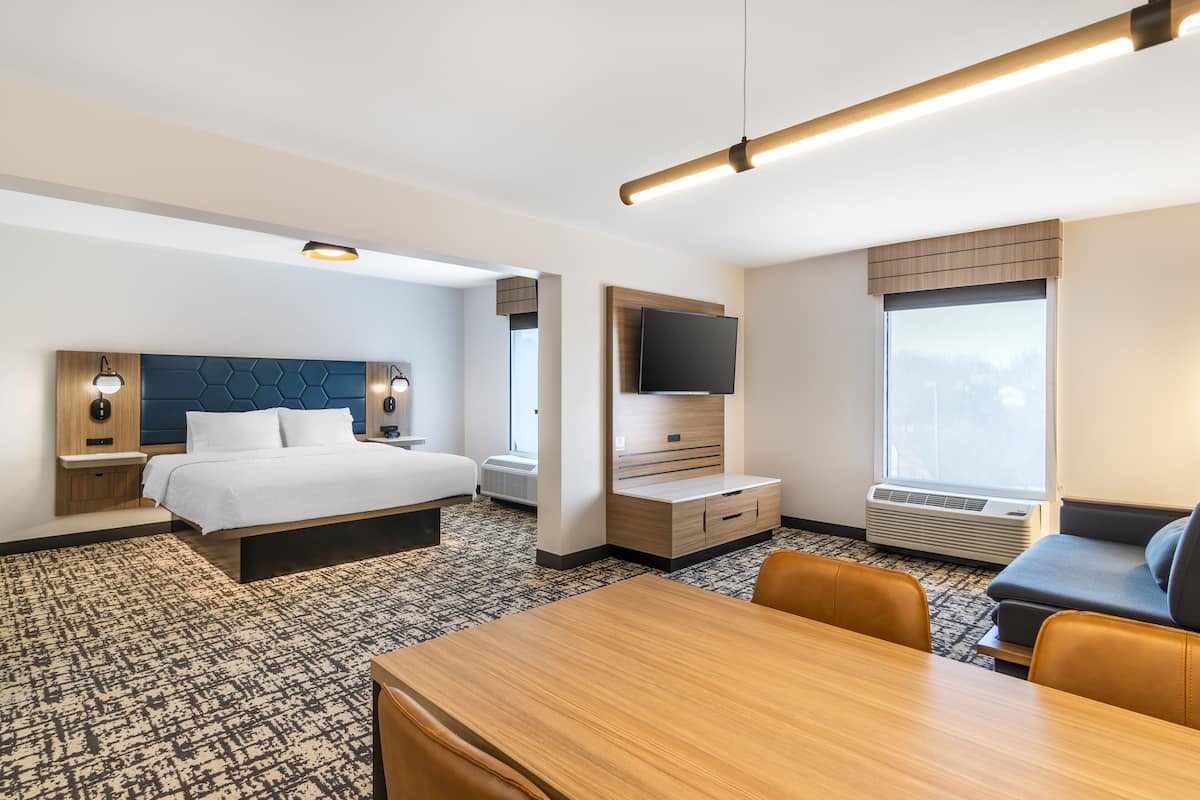 A modern hotel room with a large bed, a TV, a desk, and a seating area.