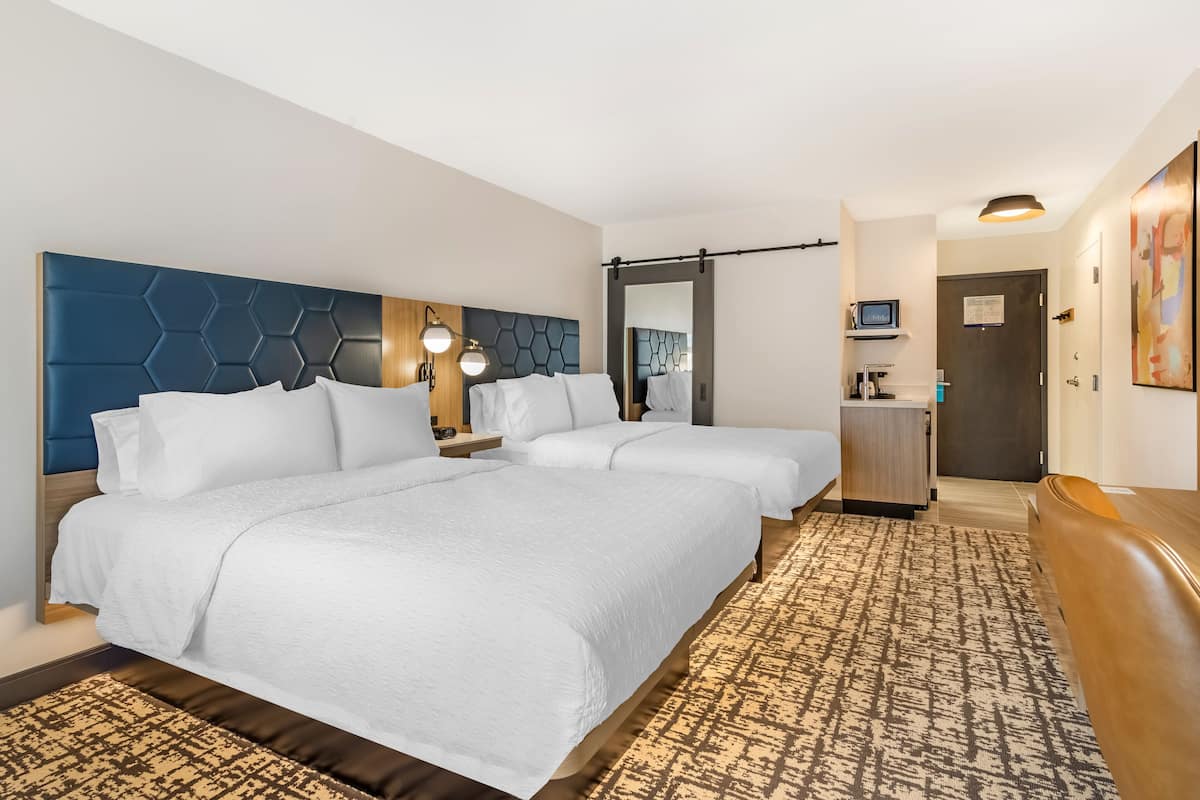 A hotel room with two beds, a desk, a mirror, and a bathroom door.