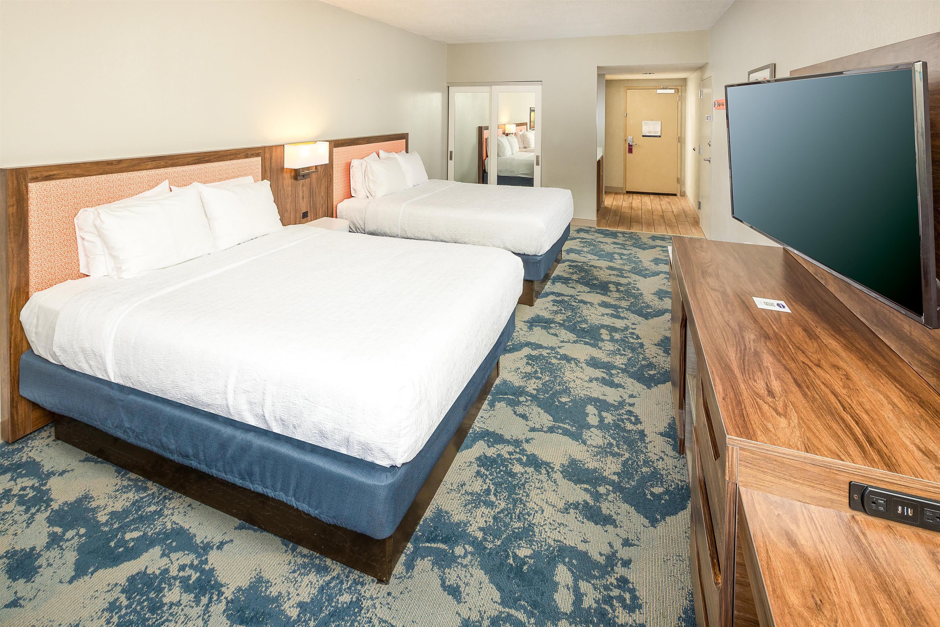 A hotel room with two beds, a desk, a television, and a carpeted floor.