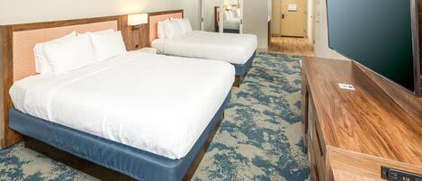 A hotel room with two beds, a desk, a television, and a carpeted floor.