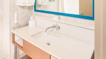 A modern bathroom with a large mirror, white sink, and neatly stacked towels.